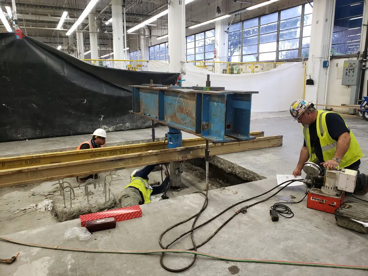 Workers and steel equipment over an opening in an industrial concrete floor